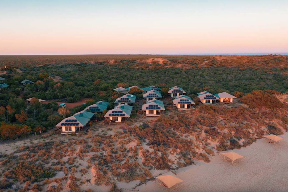 a cluster of cabins on the beach at sunset.